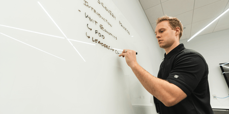Young man taking notes on a whiteboard overlaid with the text 
