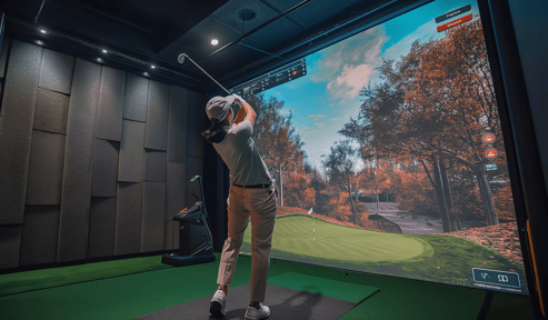 A person swinging a golf club at a simulated screen