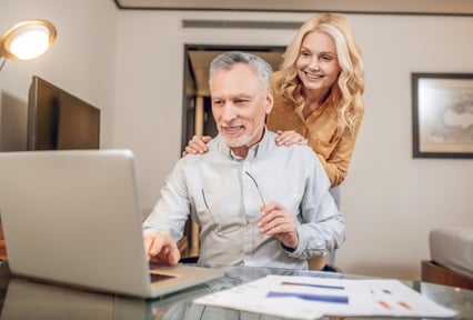 A man sitting looking at a laptop computer with a woman standing behind him