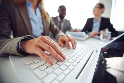 A woman typing on a keyboard with two men sitting in the background