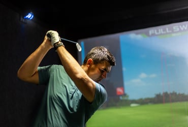 A man swinging a golf club at a simulator