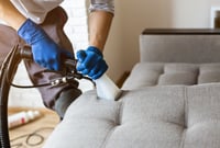 Professional cleaner using an upholstery extraction tool to deep clean a light gray fabric sofa.