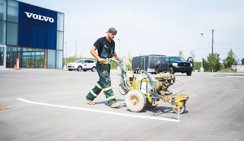 A man pushing a line painter machine in a parking lot