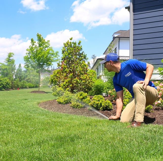 Conserva Irrigation employee inspects sprinkler system in front of a beautifully landscaped home.