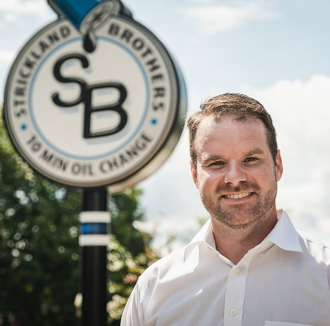 Strickland Brothers founder stands in front of Strickland Brothers 10 Minute Oil Change sign.