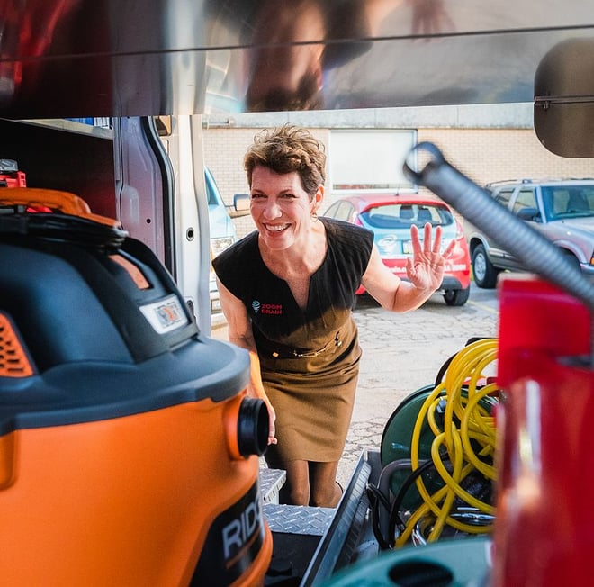 Taken from inside a Zoom Drain equipment truck looking out, Co-Founder Ellen Rohr is looking inside truck smiling and waving.