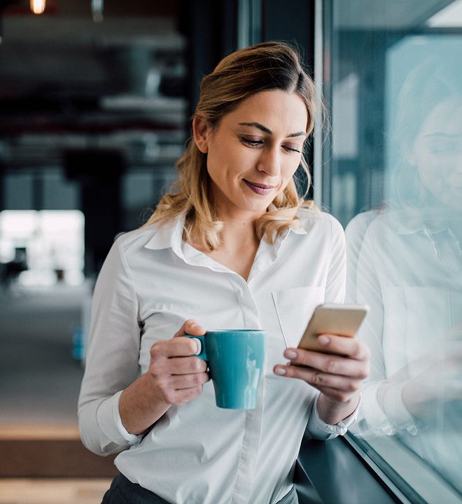 woman with coffee in hand looking at her cellphone