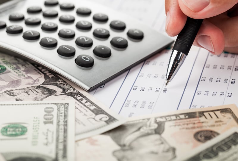 A desk with money and a calculator with a hand holding a pen
