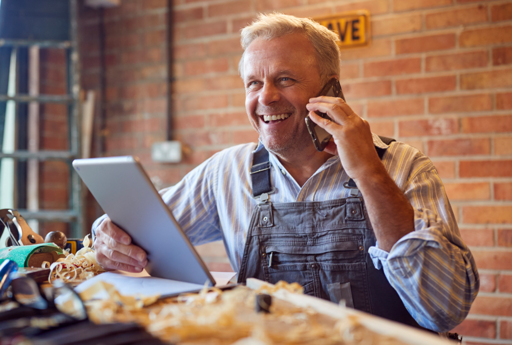 An older man smiling while on the phone holding a tablet